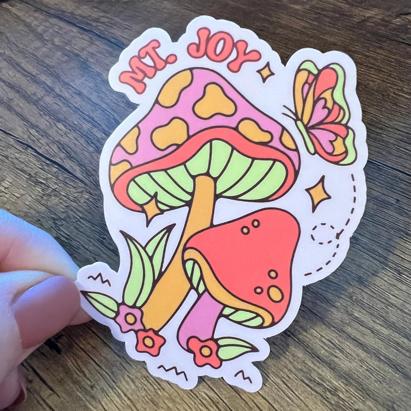 Colorful 'Mt. Joy' mushroom sticker on a wooden surface